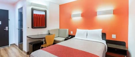 A hotel room with a bed, a desk, a chair, and a nightstand.