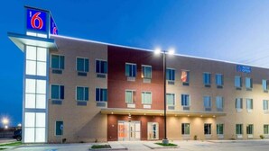 A multi-story hotel with a prominent '6' sign, a flat facade, and a 'NOW OPEN' sign indicating availability. - 1 Queen Bed|Smk| Fridge (Fort Worth)