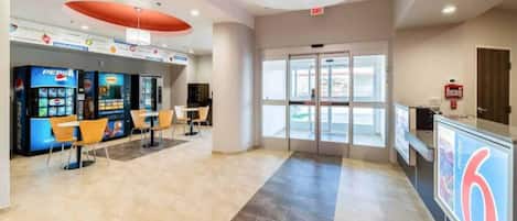 A spacious lobby with a Pepsi vending machine, seating area, and a glass door entrance.