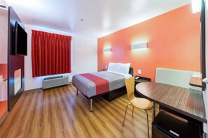 Quarto de hotel com cama, escrivaninha, cadeira, televisão e janela com cortinas.