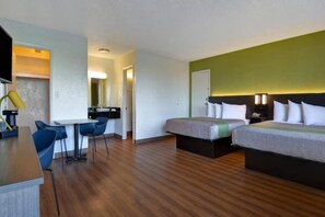 Ein Hotelzimmer mit Holzboden, einem Schreibtisch mit Stuhl, zwei Betten mit weißer Bettwäsche und einer kleinen Küchenzeile.