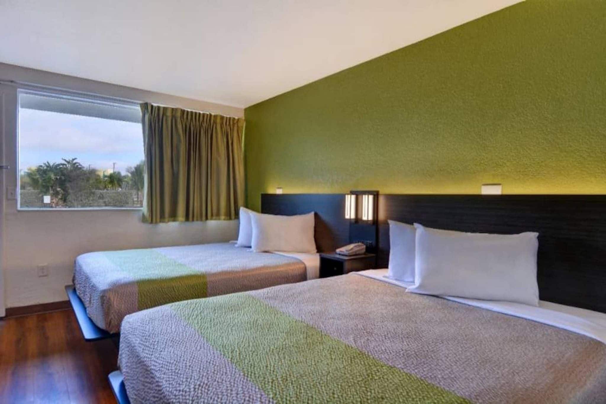 Een hotelkamer met twee bedden, een nachtkastje, een raam met gordijnen en uitzicht op de omgeving.