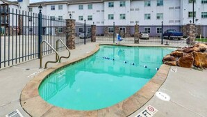 Piscina com borda curva, cercada por uma grade de metal, e um prédio com várias janelas ao fundo.