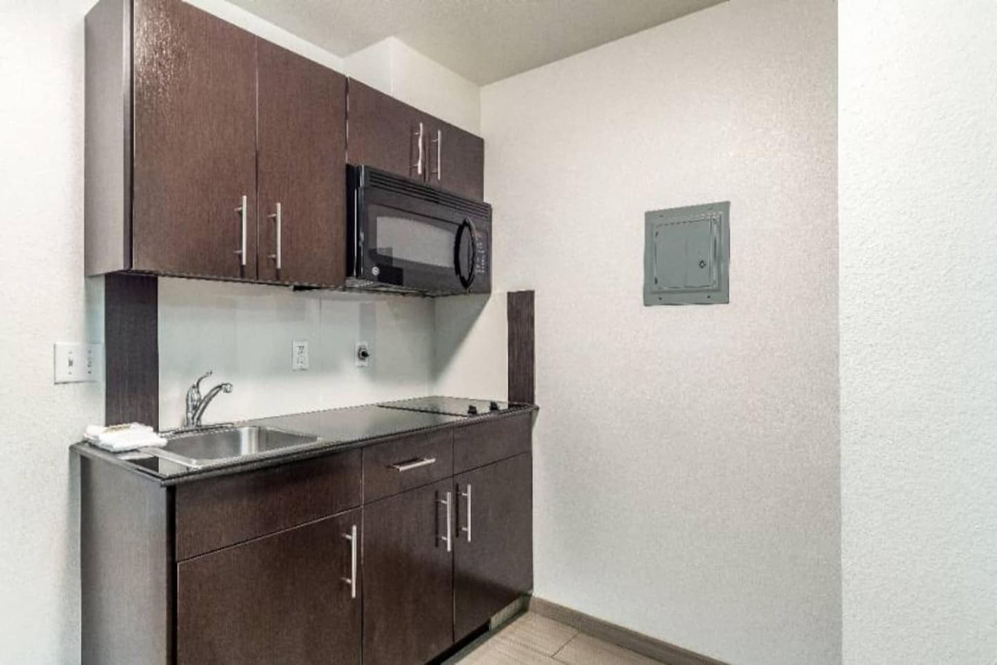 A compact kitchen with dark cabinets, a microwave, a sink, and a small electrical panel.