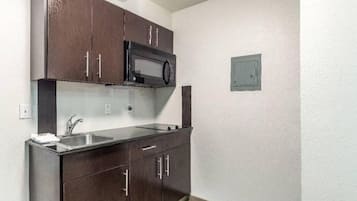 A compact kitchen with dark cabinets, a microwave, a sink, and a small electrical panel.