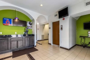 Un hall de hotel con kitchenette, televisor y un cartel que indica estadía prolongada por 6 días.
