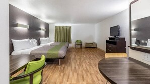 Quarto de hotel com cama, escrivaninha, cadeira, televisão e espelho.