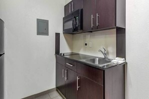 Una cocina compacta con armarios de madera oscura, un lavamanos de acero inoxidable y un microondas.