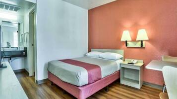 Habitación de hotel con cama, mesita de noche, lámpara y escritorio con silla.