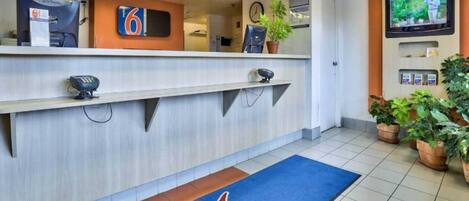Un espace d’accueil d’hôtel comprenant un comptoir, une horloge, un téléviseur et un tapis bleu orné d’un logo.