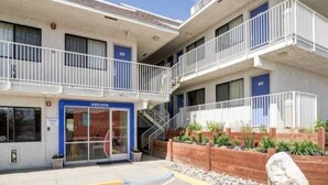 Un edificio de varios pisos con un letrero de 'Welcome', asientos exteriores y un estacionamiento.