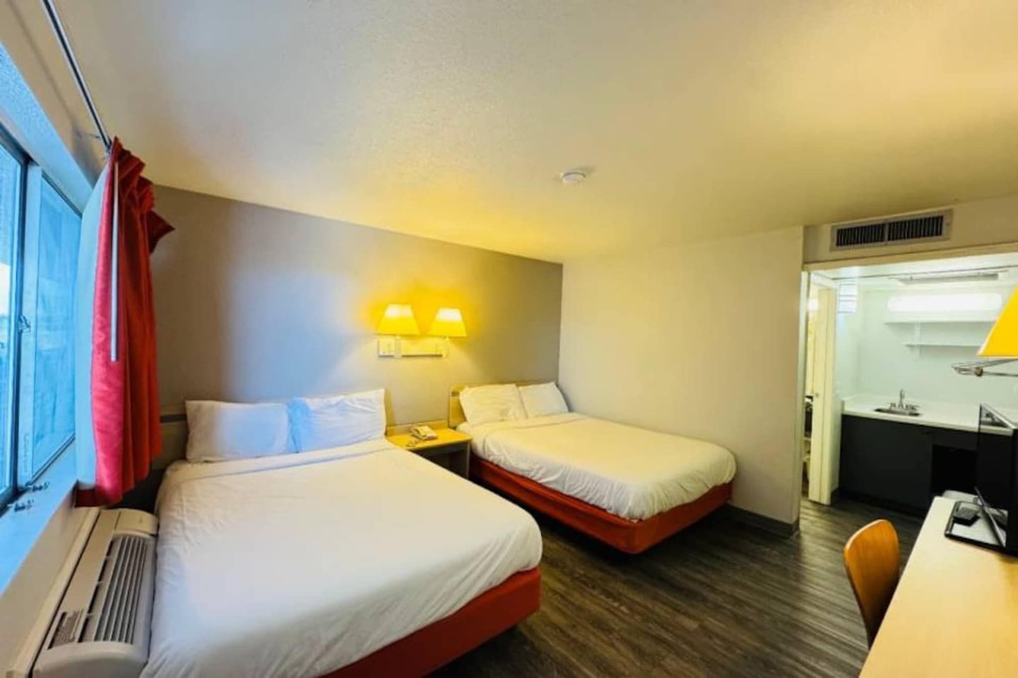 Una habitación de hotel con dos camas, un escritorio, una silla y una ventana con cortinas.