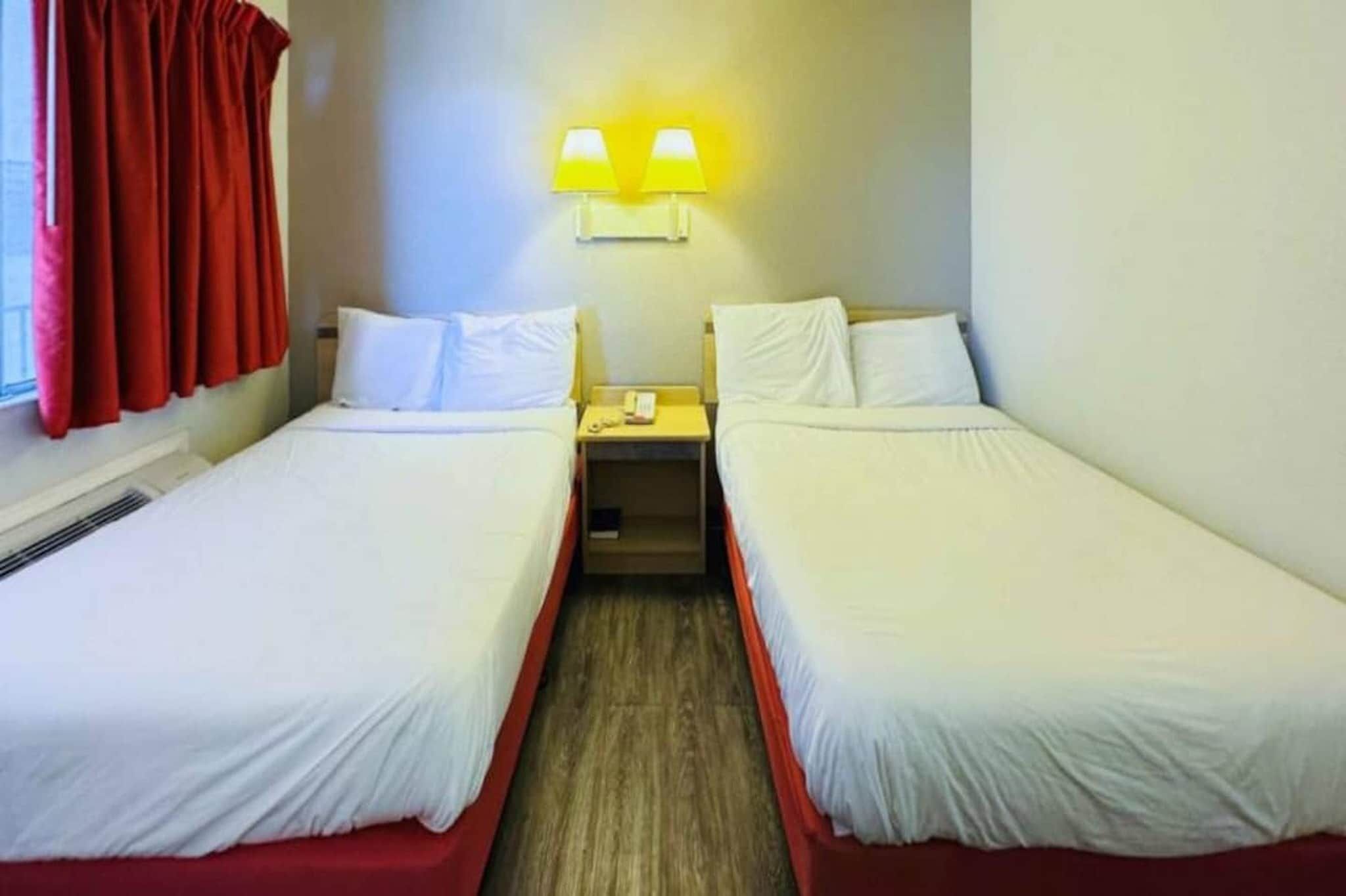 Una habitación de hotel con dos camas individuales, una mesita con teléfono y una lámpara fijada a la pared.