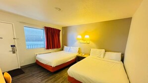 Habitación de hotel con dos camas, una ventana con cortinas, una mesita de noche con lámpara y una puerta.