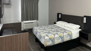 Et hotelværelse med seng, sengebord, opbevaringsplads og en varmekilde samt et vindue med gardiner.