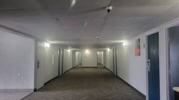 Un long couloir étroit, avec des portes de part et d’autre, un sol recouvert de moquette et un plafond où l’on peut voir les luminaires.