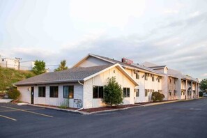 Un motel composé d’un bâtiment d’un seul étage, avec un parking à l’avant et un paysage vallonné en arrière-plan.