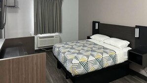 Ein Hotelzimmer mit Bett, Nachttisch, Vorhängen am Fenster, einer Wand-Klimaanlage und Holzboden.