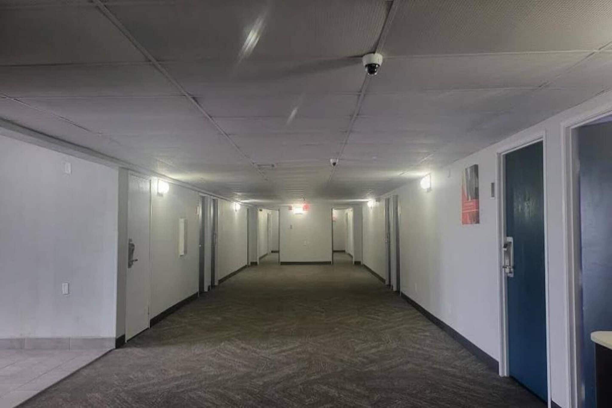 A long, narrow hallway with doors on both sides, a carpeted floor, and a ceiling with recessed lighting.