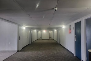 Un pasillo largo y estrecho con puertas a ambos lados, suelo alfombrado e iluminación empotrada en el techo.