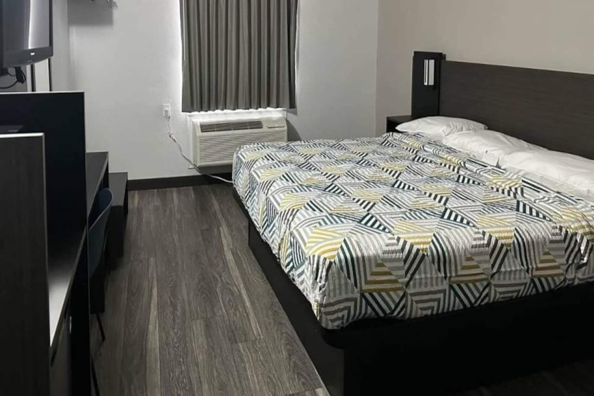 Ein Hotelzimmer mit einem Bett, einem Schreibtisch, einem Sessel, einem Fernseher und einer Klimaanlage.
