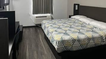 A hotel room with a bed, a desk, a chair, a television, and an air conditioning unit.