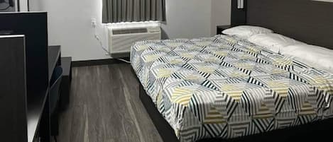 Habitación de hotel con cama, escritorio, silla, televisor y aire acondicionado.