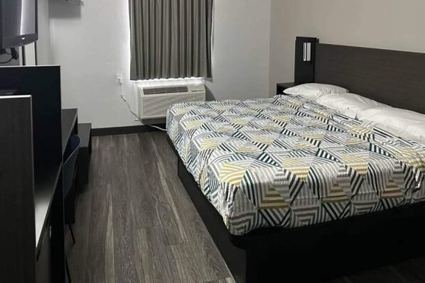 Habitación de hotel con cama, escritorio, silla, televisor y aire acondicionado.
