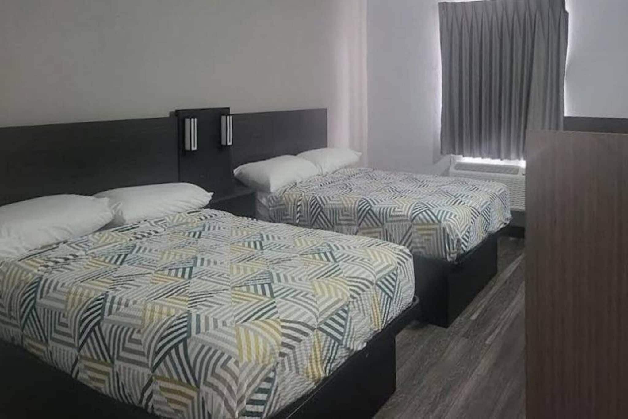Une chambre d’hôtel avec deux lits, chacun doté d’une literie à motifs, d’une tête de lit sombre et d’une fenêtre avec des rideaux.