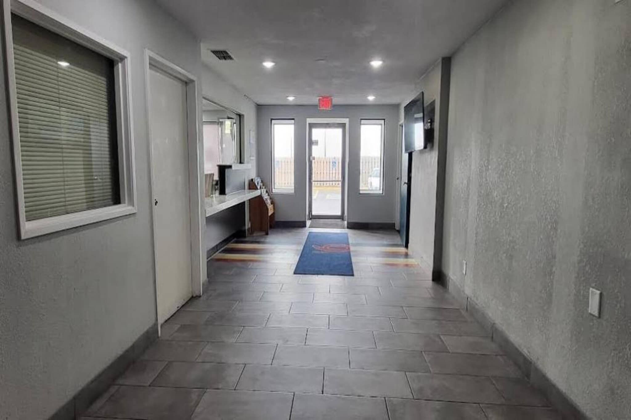 Un couloir avec un sol carrelé, un tapis bleu et une porte au fond.