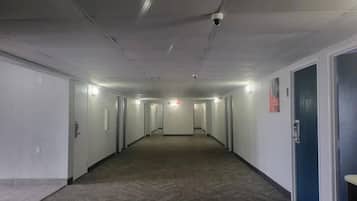 Un pasillo largo y estrecho con puertas a ambos lados, suelo alfombrado e iluminación empotrada en el techo.