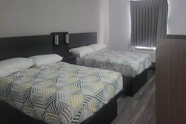 A hotel room with two beds, each with patterned bedding and a dark headboard.