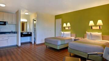 A hotel room with two beds, a kitchenette, and a bathroom.