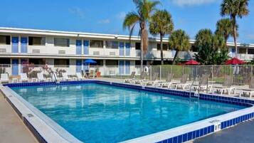A rectangular swimming pool with a blue tiled edge, surrounded by lounge chairs and a fence.