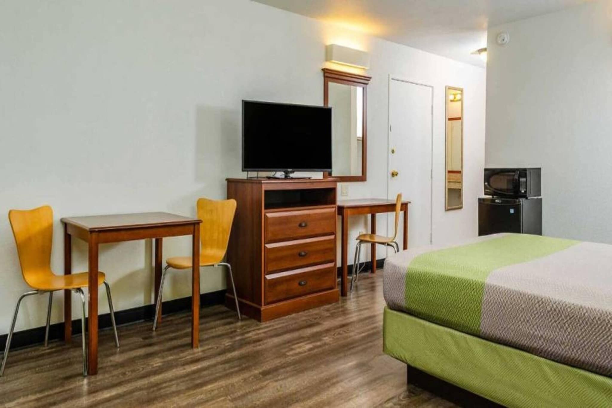 A hotel room with a bed, a desk, two chairs, a television, a dresser, a microwave, and a refrigerator.
