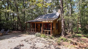 A rustic cabin with a porch, surrounded by trees.