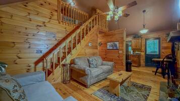 A wooden interior with a staircase, a sofa, a small table, and a ceiling fan.