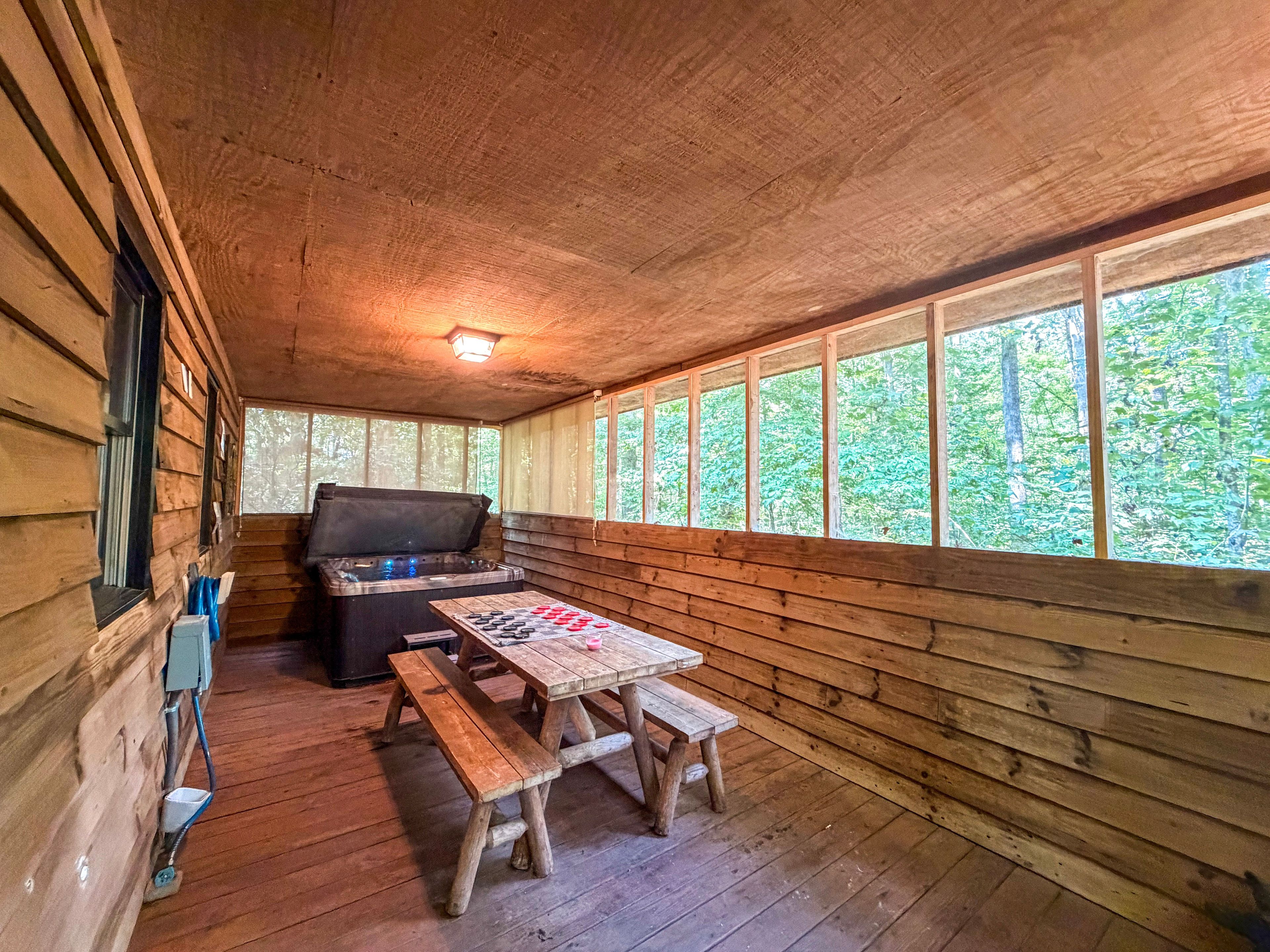 A wooden cabin with a hot tub, a picnic table, and a window overlooking a forest.