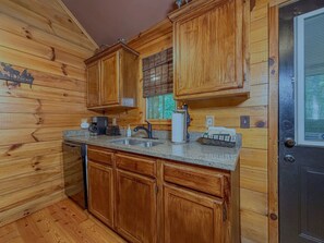 L’intérieur d’un chalet en bois comprend un coin cuisine équipé de meubles en bois, d’un plan de travail en granit, d’un évier, d’une machine à café et d’un grille-pain.