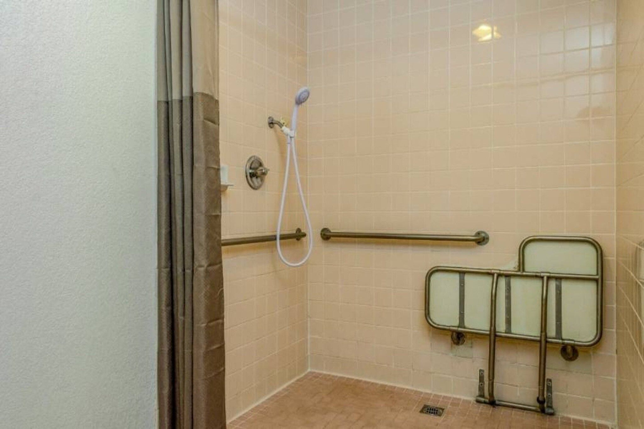 A shower area with a grab bar, a handheld showerhead, and a tiled wall.