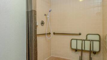 A shower area with a grab bar, a handheld showerhead, and a tiled wall.
