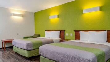 A hotel room with two beds, a small table, and a green wall with two wall-mounted lights.