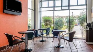 A seating area with tables and chairs, a television mounted on the wall, and a view of the outdoors through large windows.