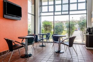 A seating area with tables and chairs, a television mounted on the wall, and a view of the outdoors through large windows. - 2 Queen Beds | Non-Smoking (OAKDALE)