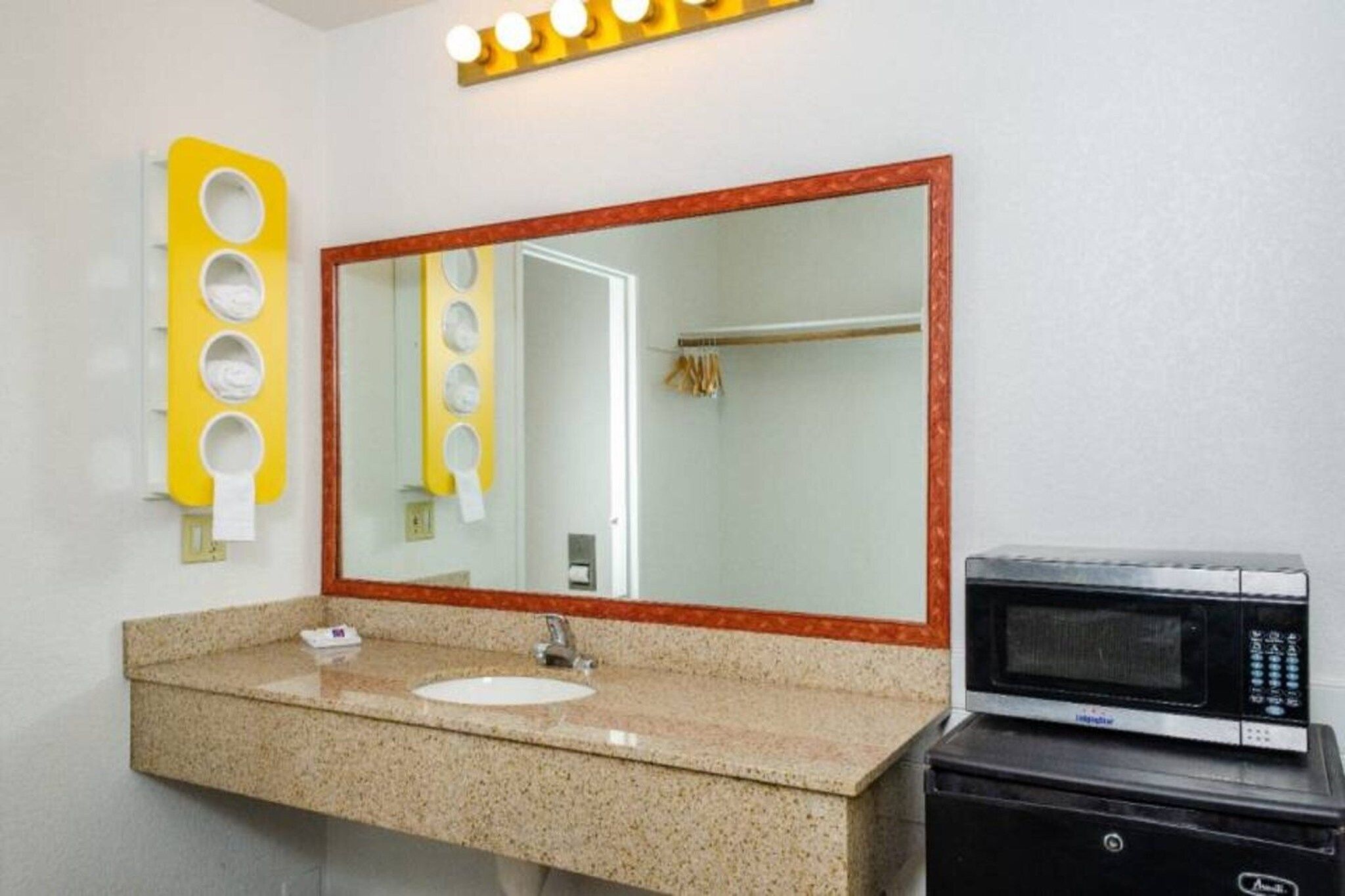 Casa de banho com bancada de granito, lavatório, espelho, porta-toalhas e micro-ondas.