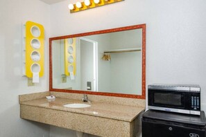 A bathroom with a granite countertop, a sink, a mirror, a towel rack, and a microwave.
