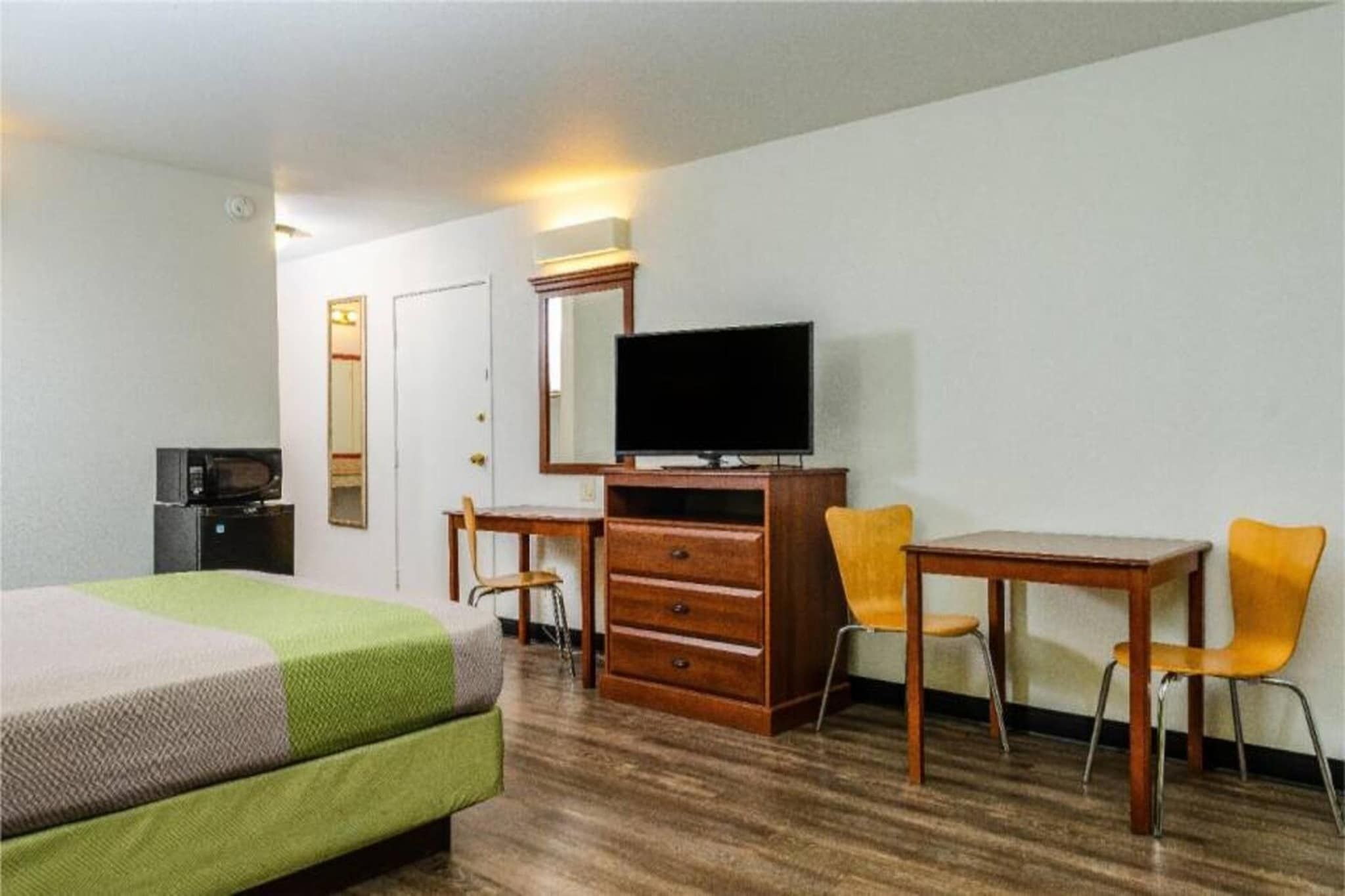 A hotel room with a bed, a desk with a television, a chair, and a dresser.