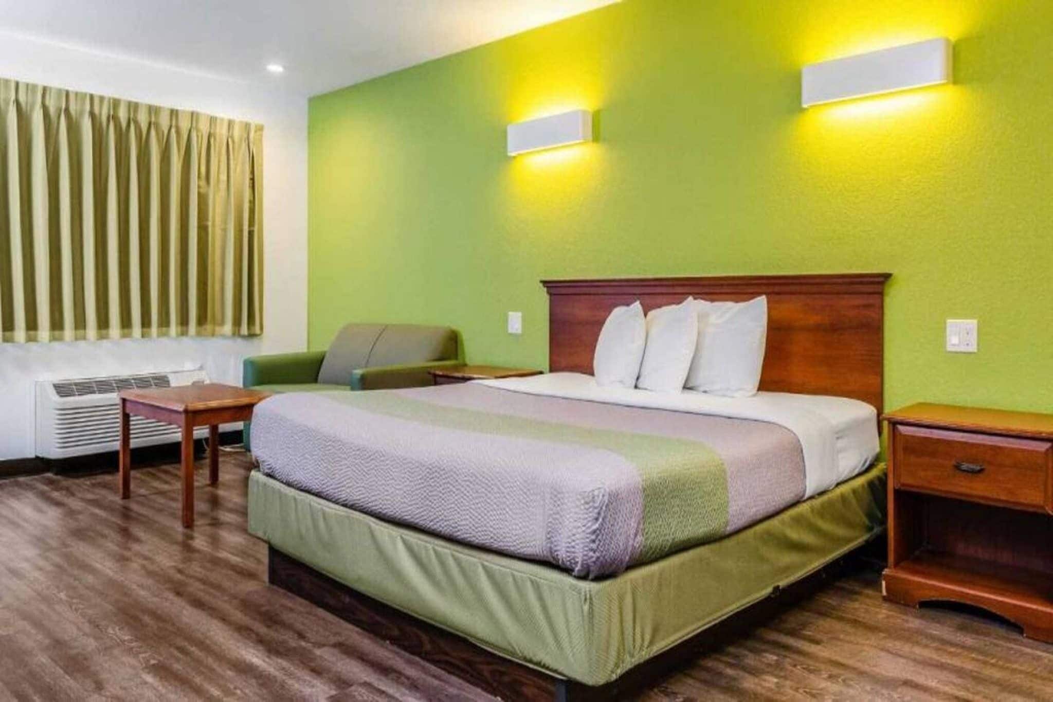 Quarto de hotel com uma cama, mesas de cabeceira, uma cadeira e uma janela com cortinas.
