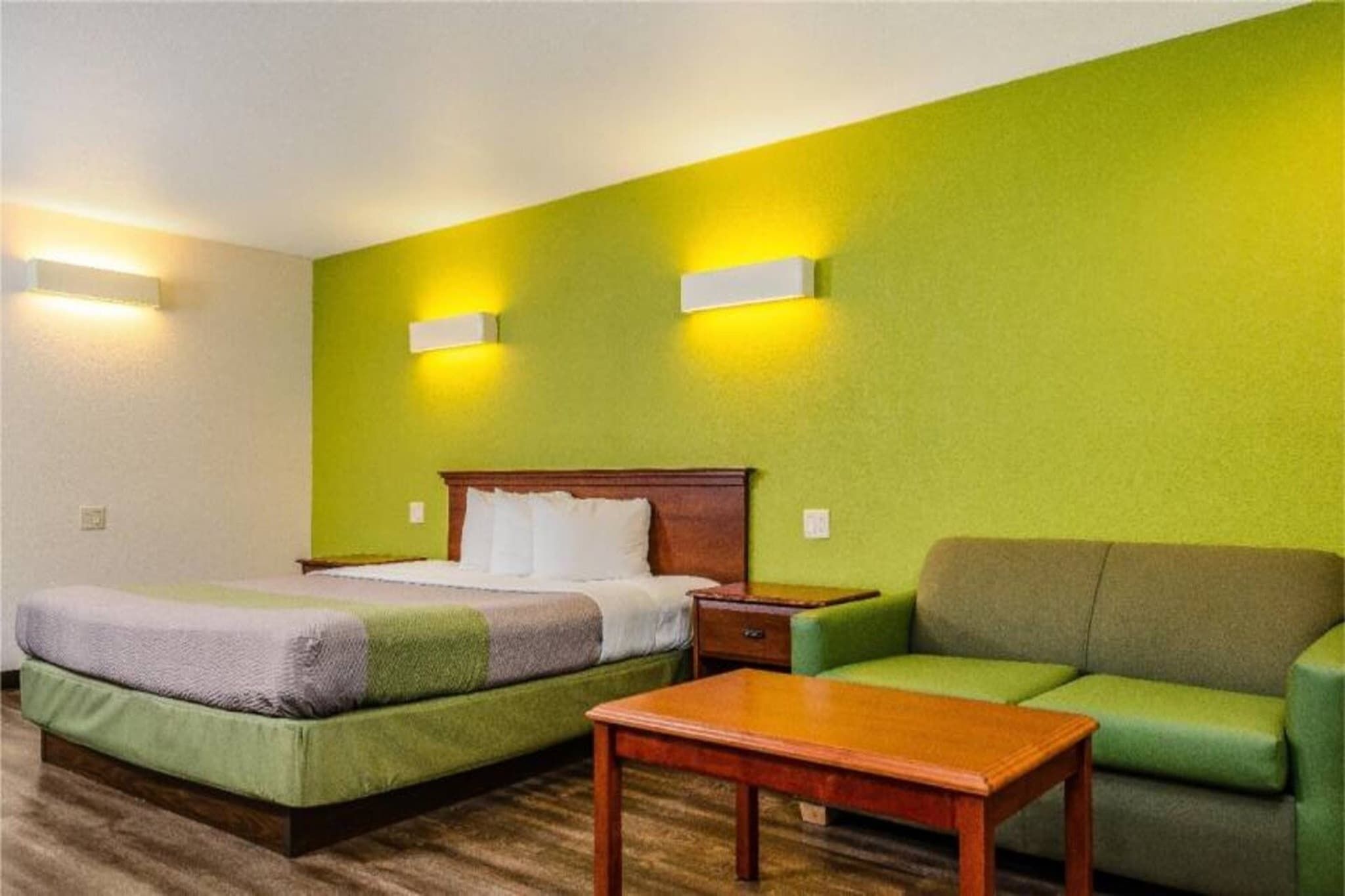Habitación de hotel con dos camas, un sofá, una mesa y dos luces empotradas.