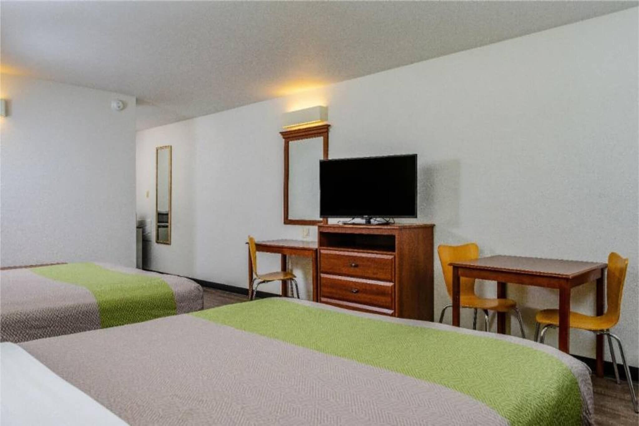 Habitación de hotel con dos camas, un escritorio, una silla, un televisor y un espejo.